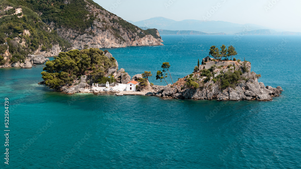 View of a crystal blue bay with a small island with a white house in colorful city Parga in Greece