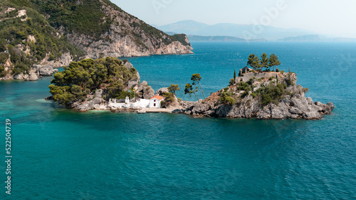 View of a crystal blue bay with a small island with a white house in colorful city Parga in Greece