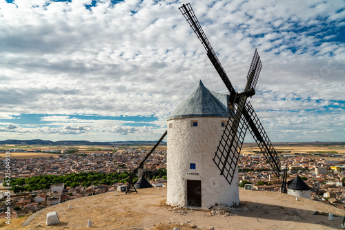 Beautiful wind mill isolated in top of a hill near to Consuegra city in Castilla-La Mancha - Spain. Cloudy day. In background the city of Consuegra. The land of Don Quixote