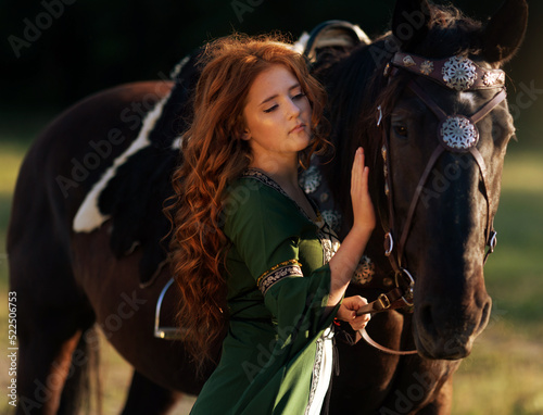 Medieval woman princess in green dress sits astride black steed horse.