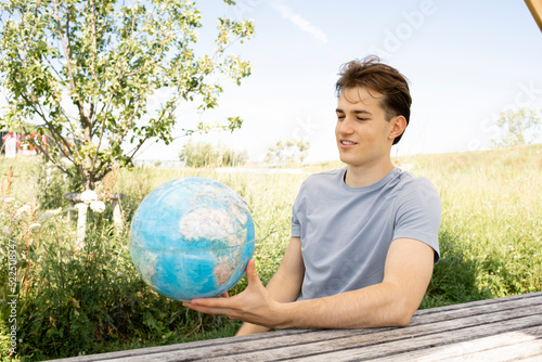 teenager with grey shirt sitting on park bench holding globe in his hand and dreaming of a trip, vacation