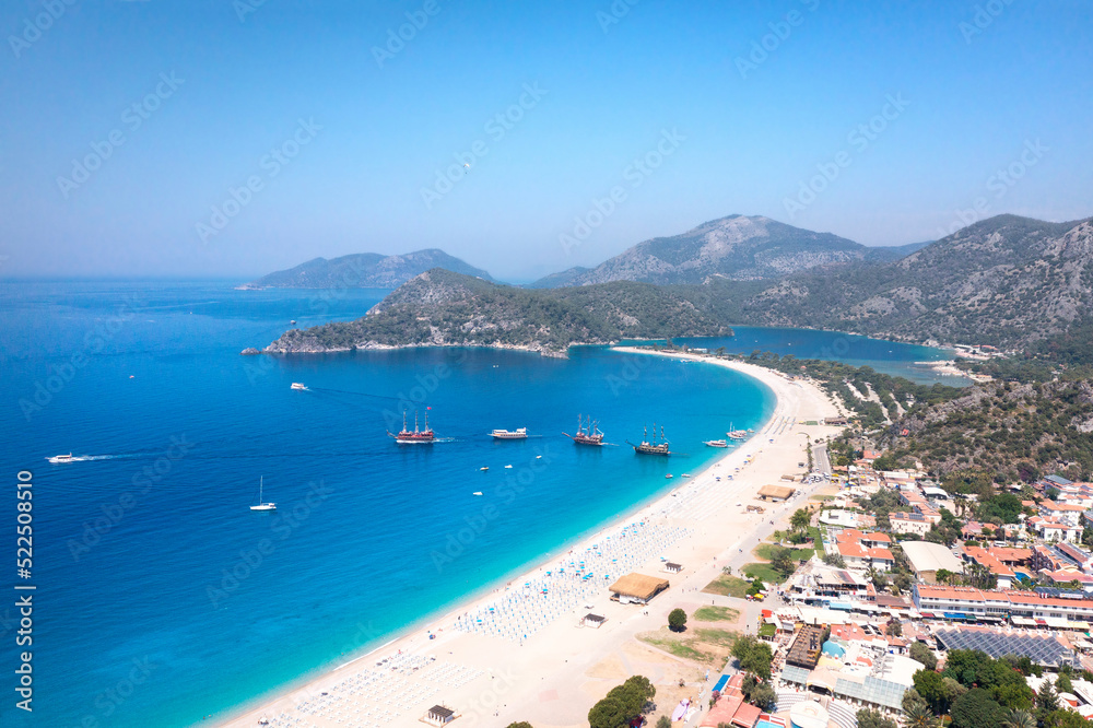 Aerial view of beautiful coasline with white sand and blue water close to Fethiye, Oludeniz. Tourist ships sail from the shore into the open sea. Famous place sports paragliding. 
