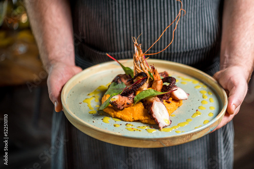 Fototapeta Naklejka Na Ścianę i Meble -  Chef holding delicious seafood platter with lobster and octopus on pumpkin pillow