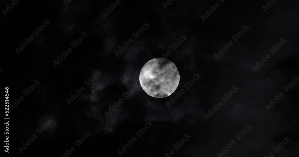 Full moon at night. The illuminated face of the moon is wrapped in a cloud cover that covers it in a veiled way. Full moon at night. The illuminated face of the moon is wrapped in a cloud cover that covers it in a veiled way.