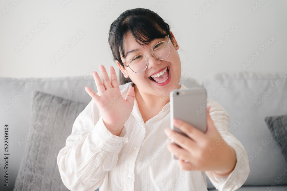 Young Asian woman using smartphone for online video conference call with friends waving hand making hello gesture Young Asian woman using smartphone for online video conference call with friends waving hand making hello gesture