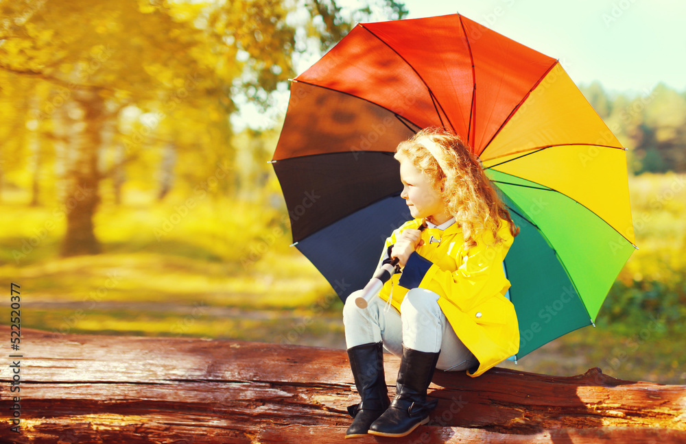Obraz premium Happy little girl child with colorful umbrella in sunny autumn park
