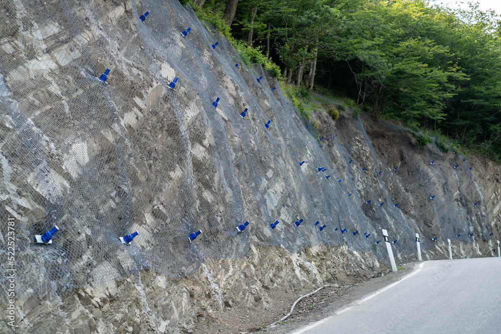 Reinforcing mountain slope with metal mesh and concrete reinforcement, preventing rocks falling on the road. Landslide and rock sliding prevention in Georgia. Cliff erosion control concept.  - obrazy, fototapety, plakaty 