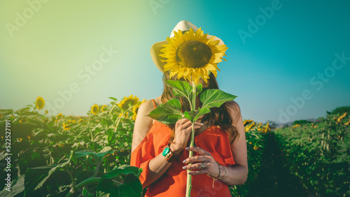 Mujer sosteniendo un girasol para cubrir su rostro en un dia soleado
