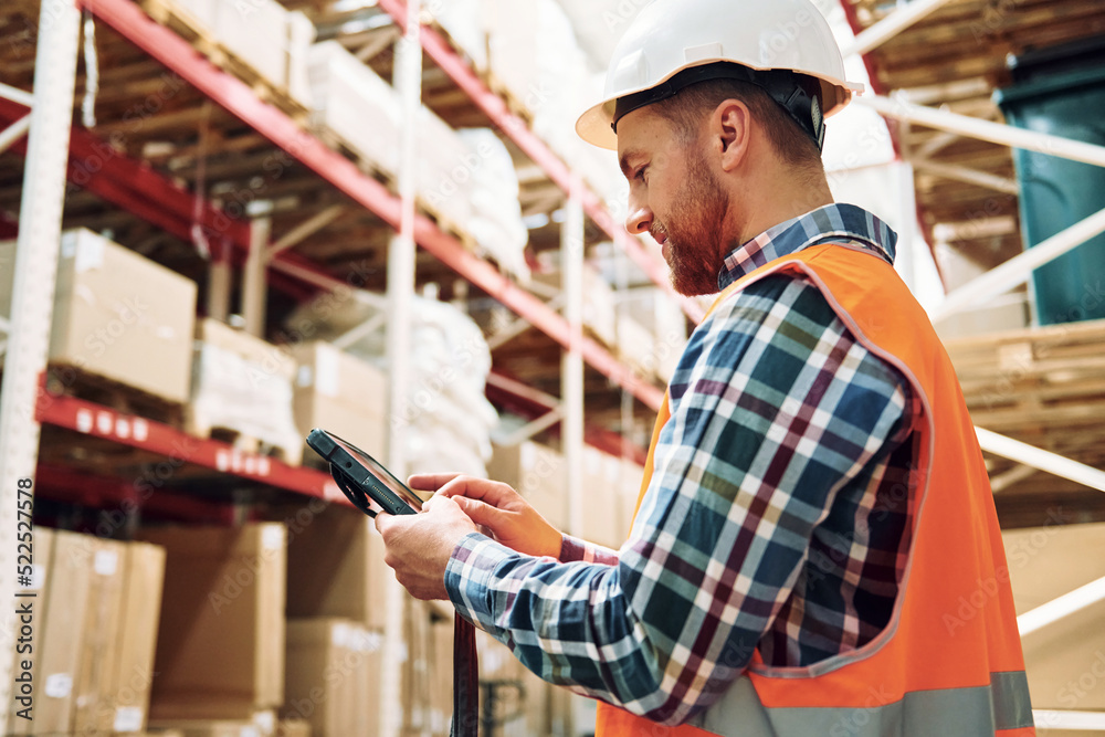 Holding tablet in hands. Employee in uniform is working in the storage at daytime Holding tablet in hands. Employee in uniform is working in the storage at daytime