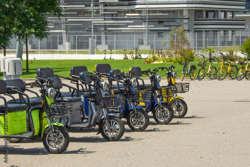 Electric scooters, three-seater mopeds at the parking lot for rental and movement around the city.