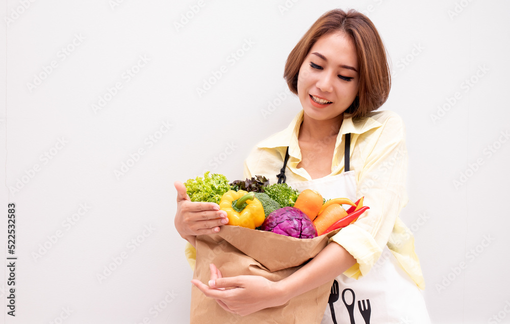 Young smiling Asian cheerful happy fun vegetarian woman 20s in casual clothes hold paper bag with vegetables after shopping look camera isolated on plain yellow background studio portrait. Young smiling Asian cheerful happy fun vegetarian woman 20s in casual clothes hold paper bag with vegetables after shopping look camera isolated on plain yellow background studio portrait.