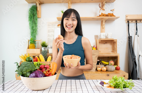 Asian Fitness woman is showing off chicken eggs. She stands with them in her hands and a kitchen in the background. Smiling Woman Holding Egg. Fitness woman prepare healthy breakfast.