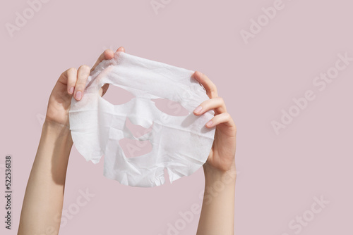 Female hands holding sheet of white mask on pink background. photo