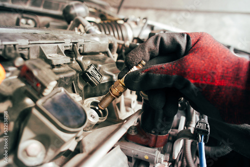 A auto mechanic is installing automobile iridium spark plugs into the ignition socket of the engine block in the engine compartment.