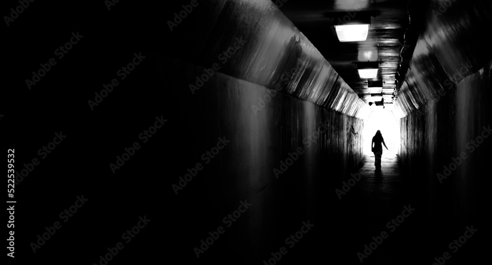 Fototapeta premium Person walking through tunnel towards light at end. Accomplishing goal or leaving darknenss for light.