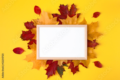 Empty wooden frame mock up and autumn leaves on yellow background. Template for design.