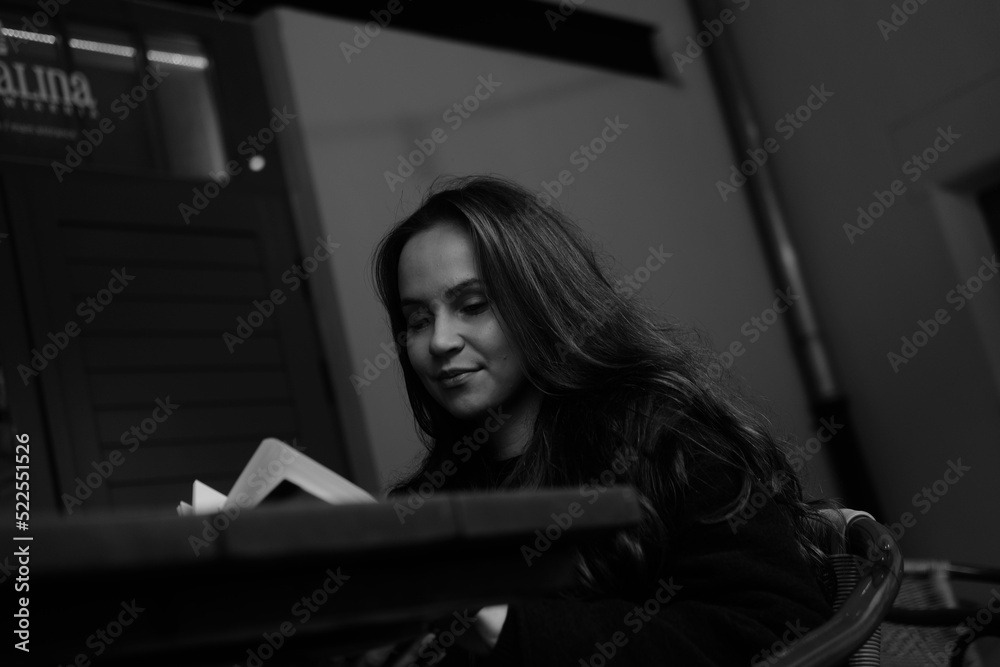 Black and white portrait of a young brunette girl with a book in her hands. Women is siting in the chair Black and white portrait of a young brunette girl with a book in her hands. Women is siting in the chair