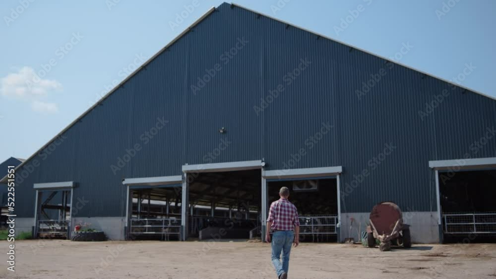 Farmer going modern barn producing organic food. Specialist walking to farm.