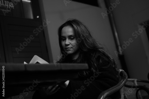 Black and white portrait of a young brunette girl with a book in her hands. Women is siting in the chair 