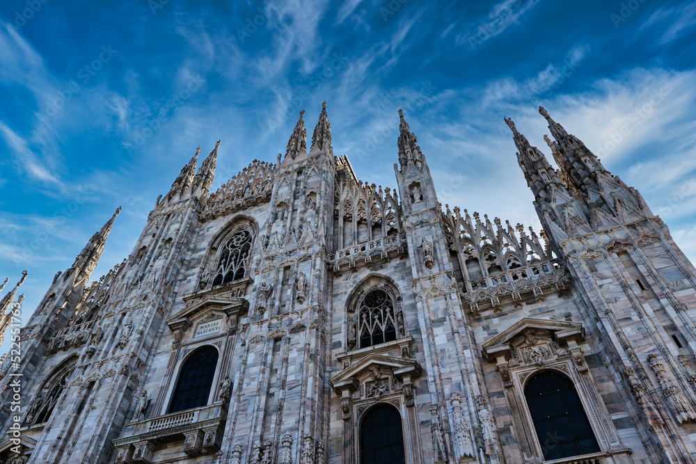 Frontview of the multiple small towers and detailed decoration of the Milan Cathedral. Sunlight comes from behind in the morning with a dramatic sky background. Historical cathedral in Milan, Italy. 