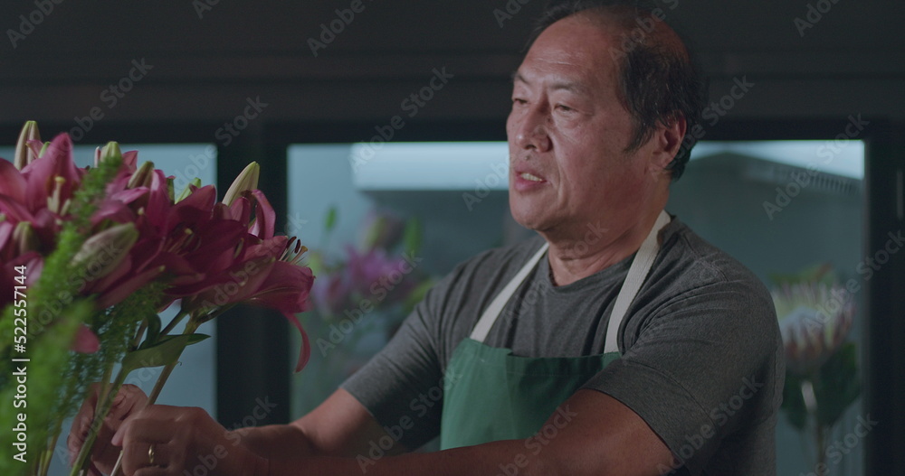 Fototapeta premium An Asian American florist preparing bouquet of flowers for online delivery. Portrait of an artisan male florist creating artistic arrangement for client at flower shop