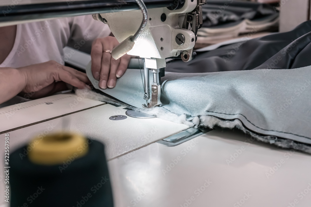 The seamstress sews at the sewing machine, threads the fabric. Women's hands