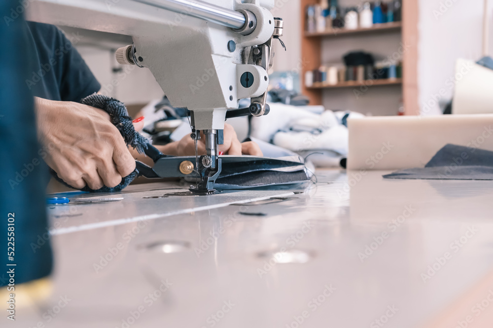 A seamstress cuts fabric while working at a sewing machine in the workshop. Women's hands