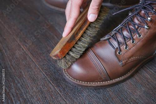 close up of hand with shoe brush brushing shine fashion leather boot on wooden floor