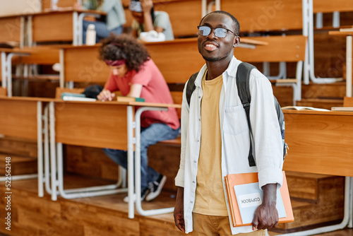 Portrait of African student in eyeglasses with backpack smiling at camera standing at auditorium of university © AnnaStills