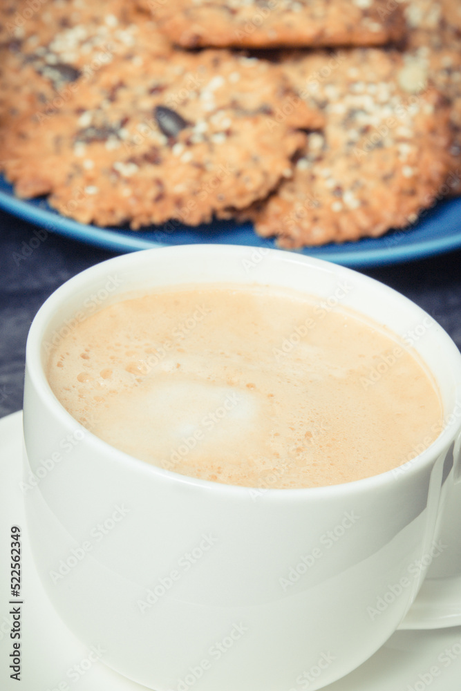 Cup of white coffee and fresh baked oatmeal cookies with honey and healthy seeds on blue plate. Delicious crunchy dessert Cup of white coffee and fresh baked oatmeal cookies with honey and healthy seeds on blue plate. Delicious crunchy dessert