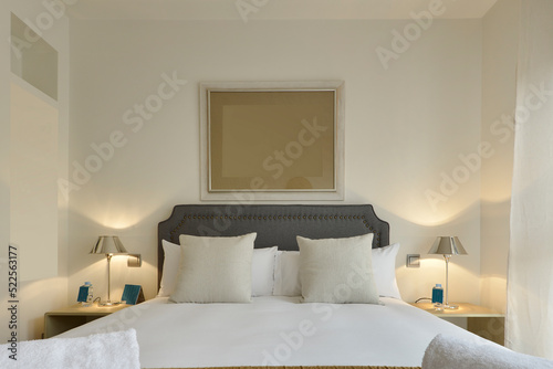 Bedroom with headboard upholstered in blue fabric, pillows and cushions and twin chrome metal lamps