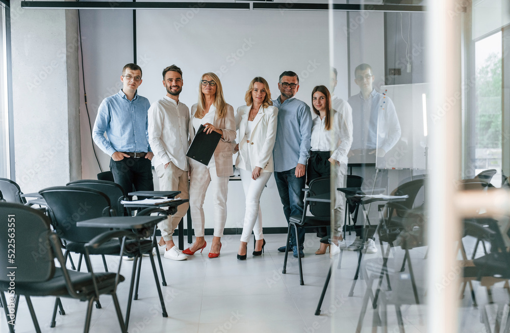 Standing and posing for a camera in the class. Group of professional business people is in the office Standing and posing for a camera in the class. Group of professional business people is in the office