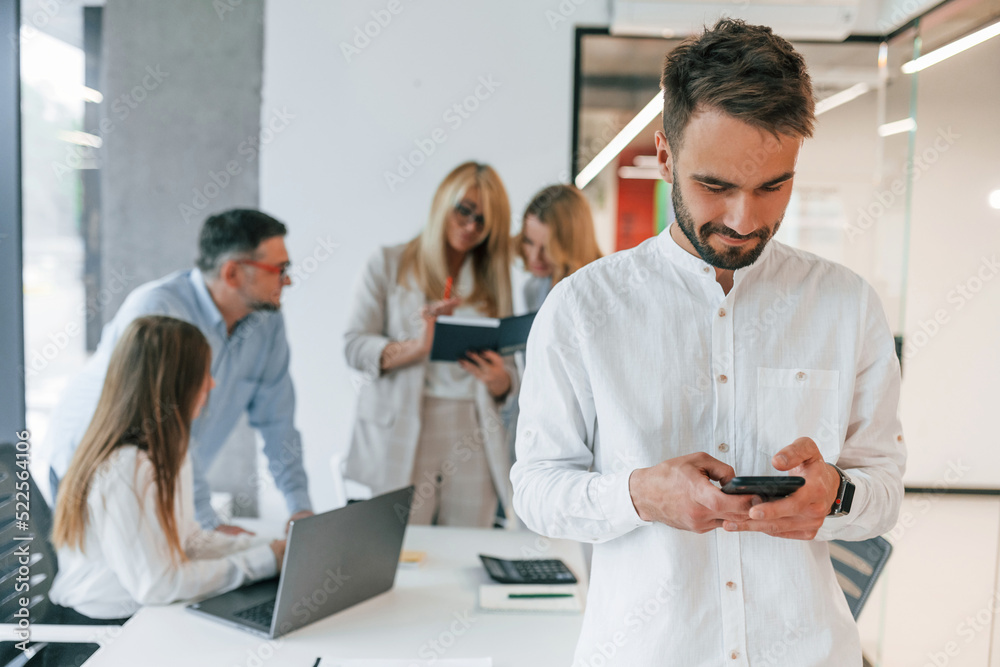 Beautiful cheerful man posing for the camera. Group of professional business people is in the office Beautiful cheerful man posing for the camera. Group of professional business people is in the office