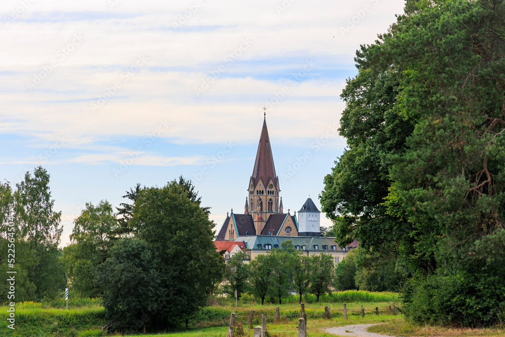 The church tower of St. Ottilien Monastery in Bavaria between forests and meadows under white blue sky