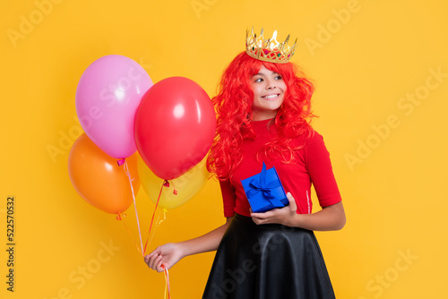 cheerful child in crown with present and party balloon on yellow background