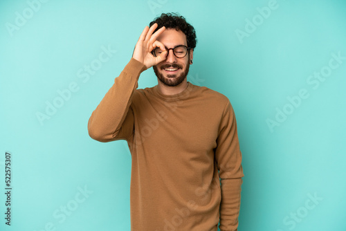 Fotografie young bearded man smiling happily with funny face, joking and looking through pe