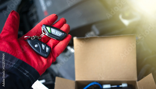 Installing an anti-theft alarm in the car.A gloved hand holds an alarm keychain against the open hood of a car.