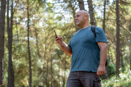 Hiker man lost in the forest, uses the phone to guide himself and find the way.