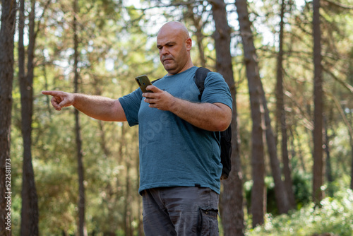 Hiker man lost in the forest, uses the phone to guide himself and find the way.