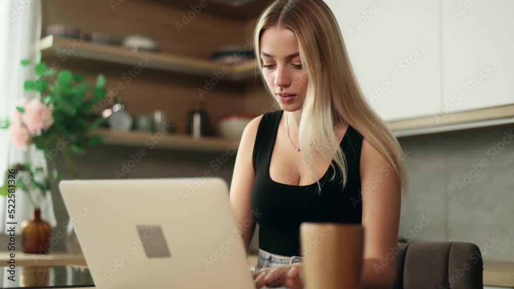 Smiling young woman with laptop using laptop in the kitchen. Happy young woman with computer, freelancer working at home. Smiling young woman with laptop using laptop in the kitchen. Happy young woman with computer, freelancer working at home.