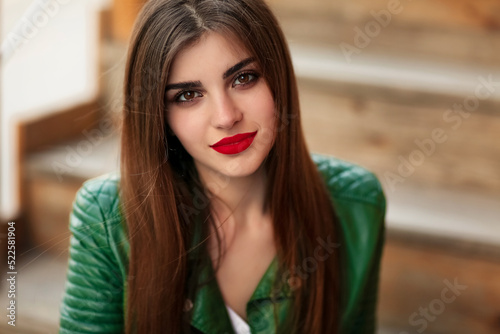 Fashion outdoor portrait of gorgeous long hair woman in green leather jacket and red lips, autumn style. Fashionable hipster girl in trendy casual clothes posing at city street lifestyle.