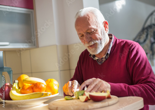 Senior man eating fruits in the kitchen on a sunny day