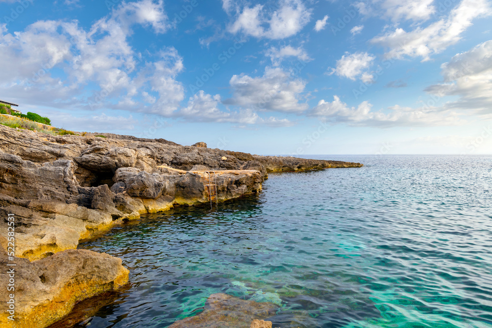 The rocky coastline of Binibeca Vell, Spain, with a ladder on the rocks into the shallow waters on the island of Menorca, Spain.