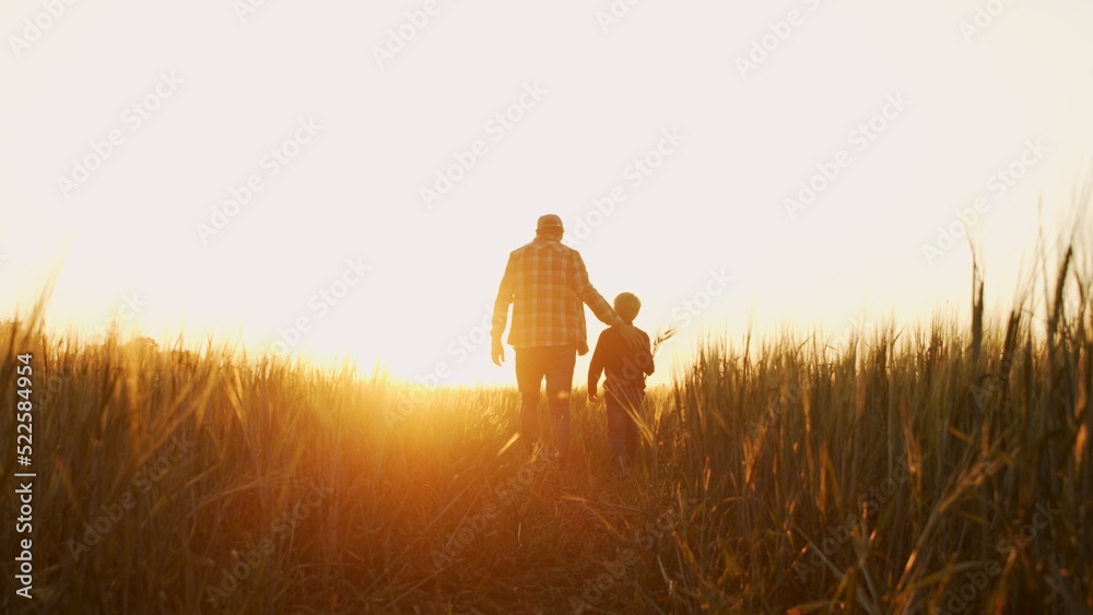 Farmer and his son in front of a sunset agricultural landscape. Man and a boy in a countryside field. Fatherhood, country life, farming and country lifestyle. - obrazy, fototapety, plakaty 