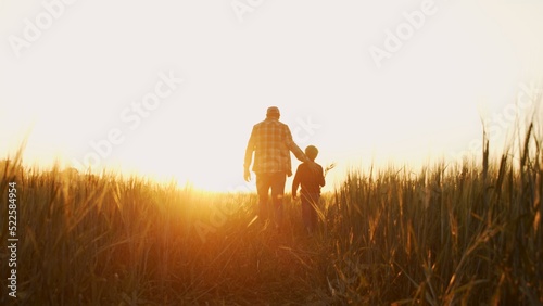 Leinwand Poster Farmer and his son in front of a sunset agricultural landscape