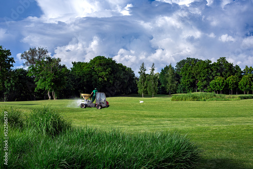 transport specialized equipment for fertilization and lawn care on a golf course, gardening supplying plants with nutrients on a hilly landscape on a sunny day with clouds on the sky.