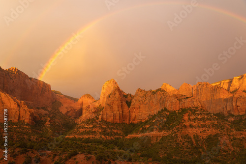 The setting sun paints the mountains of Kolob fingers on the northwestern side of Zion National park, Utah and a rainbow forms in the clouds after a summer monsoon storm has rolled through. 