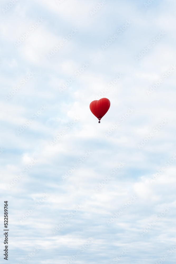 Red hot air balloon in shape of heart is landing on the green field