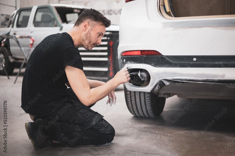 A mechanic going over a car bumper with sandpaper. Stock Photo Adobe