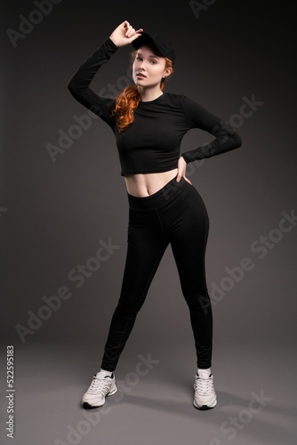 Stylish redhead lady adjusting cap and show at camera in studio